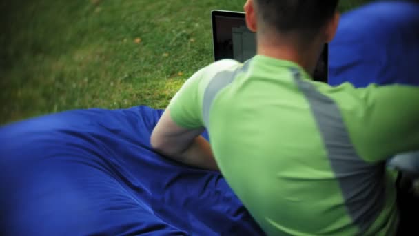 Ein älterer Mann benutzt einen Laptop, der in einem Aufenthaltsraum des Parks auf weichen Windbeutel liegt — Stockvideo