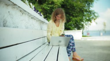 Park ahşap bir bankta bir dizüstü bilgisayar üzerinde çalışan güzel kadın