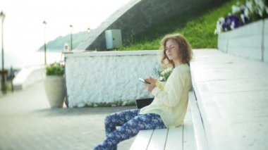 Güzel kadın parkta ahşap bir bankta bir akıllı telefon kullanır
