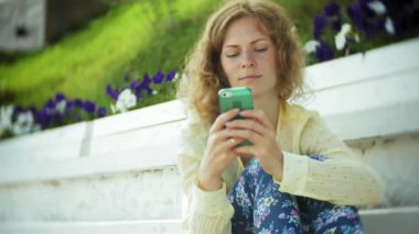 Güzel kadın parkta ahşap bir bankta bir akıllı telefon kullanır