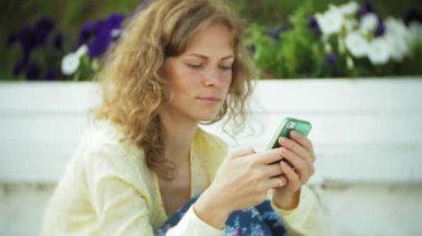 Güzel kadın parkta ahşap bir bankta bir akıllı telefon kullanır