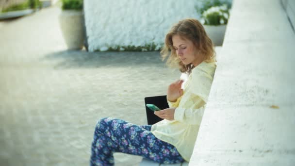 Belle femme utilise un smartphone sur un banc en bois dans le parc — Video