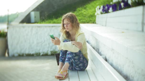 Güzel kadın parkta ahşap bir bankta bir akıllı telefon kullanır — Stok video