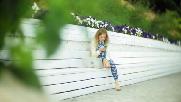 美丽的女人在公园的木凳上使用智能手机4K — 图库视频影像