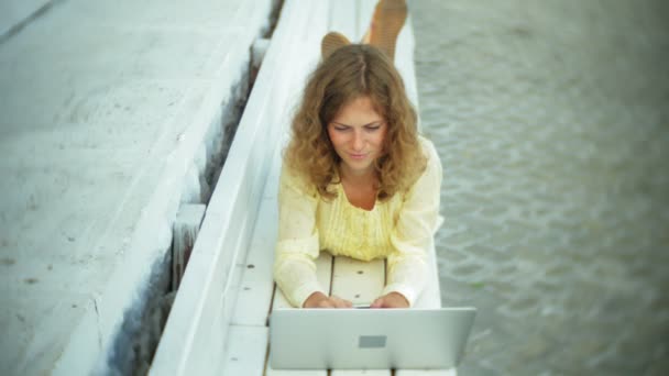 Belle femme travaillant sur un ordinateur portable sur un banc en bois dans le parc — Video