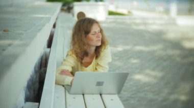 Park ahşap bir bankta bir dizüstü bilgisayar üzerinde çalışan güzel kadın