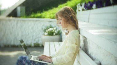 Park ahşap bir bankta bir dizüstü bilgisayar üzerinde çalışan güzel kadın