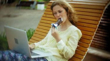 Güzel kadın bir dondurma yiyor ve Park ahşap bir bankta bir dizüstü bilgisayarda çalışır