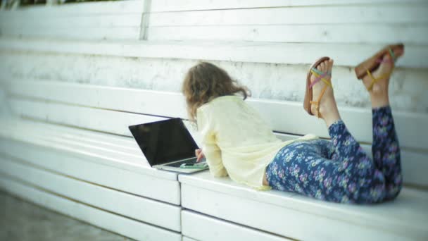 Bella donna che lavora su un computer portatile su una panchina di legno nel parco — Video Stock
