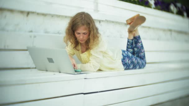 Красивая женщина работает на ноутбуке на деревянной скамейке в парке — стоковое видео