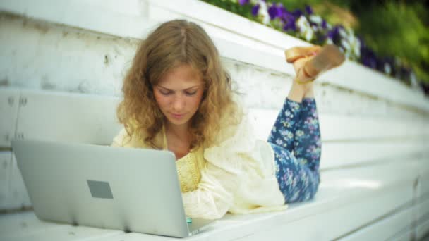 Belle femme travaillant sur un ordinateur portable sur un banc en bois dans le parc — Video