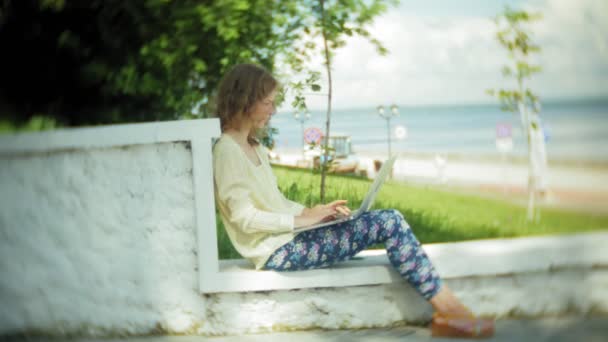 Működő-ra egy laptop, egy fa pad a parkban a gyönyörű nő — Stock videók