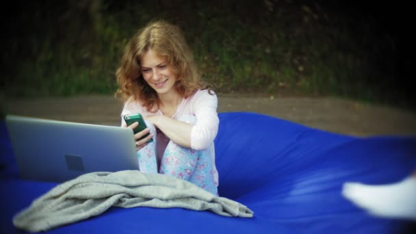 Young woman uses a smartphone, lying in the lounge area of the park on soft puffs — Stock Video