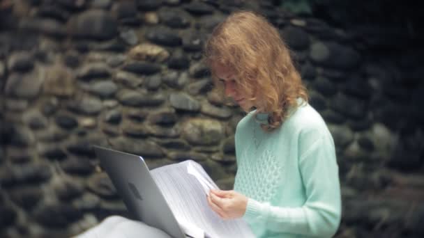 Γυναίκα με φορητό υπολογιστή και έγγραφα σχετικά με το φόντο ενός τοίχου stonewall — Αρχείο Βίντεο