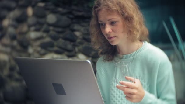 Vrouw met een laptop en documenten op de achtergrond van een stenen muur. Dranken en wijn drinkt uit een glas — Stockvideo