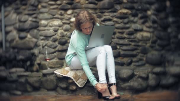 Женщина с ноутбуком и документами на фоне каменной стены. Напитки и напитки из бокала — стоковое видео