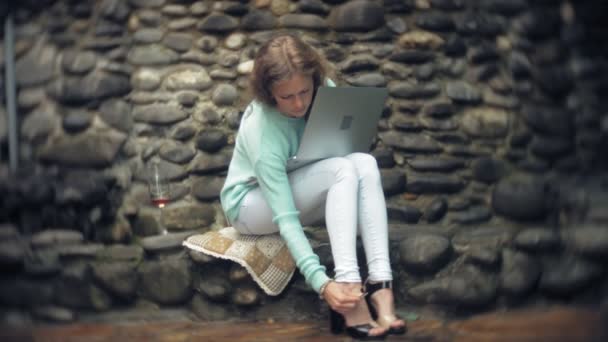 Mujer con un portátil y documentos en el fondo de una pared de piedra. Bebidas y bebidas vino de una copa — Vídeos de Stock