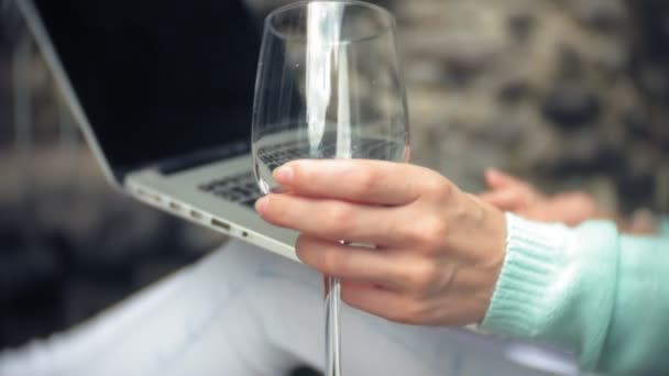 ノート パソコンと石壁の背景上のドキュメントとの女性。飲み物し、グラスからワインを飲む — ストック動画