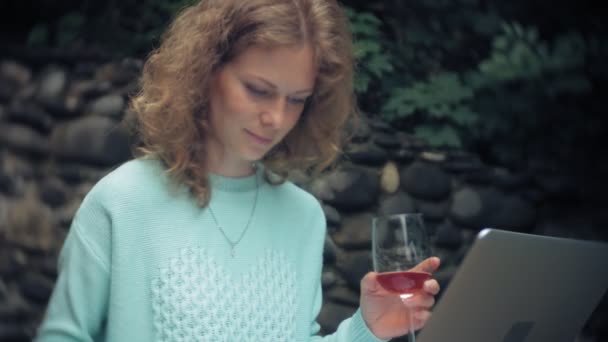 Mujer con un portátil y documentos en el fondo de una pared de piedra. Bebidas y bebidas vino de una copa — Vídeos de Stock