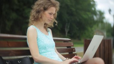 Sahilde bir dizüstü bilgisayar kullanarak bir bankta oturan bir kadın