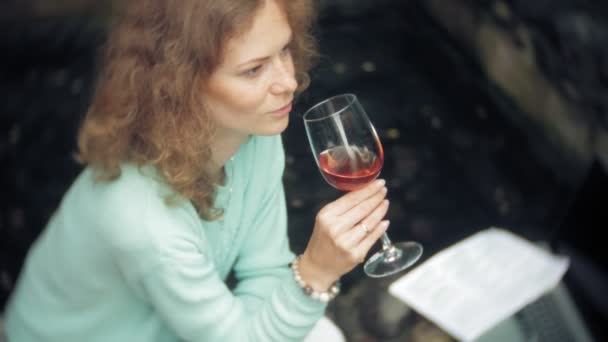 Žena s notebookem a dokumenty na pozadí kamenné zdi. Pije a pije víno ze skla — Stock video