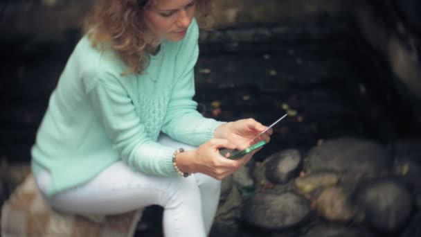 Uma mulher está usando um smartphone contra uma parede traseira. Bebidas e bebidas vinho de um copo — Vídeo de Stock