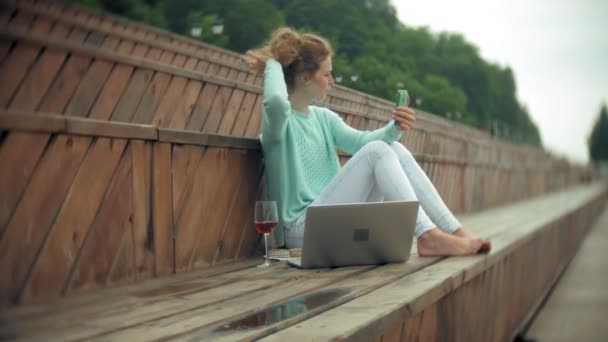 Uma mulher com um portátil e documentos. Bebidas e bebidas vinho de um copo — Vídeo de Stock