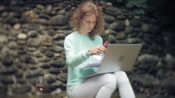 Vrouw met een laptop en documenten op de achtergrond van een stenen muur. Dranken en wijn drinkt uit een glas — Stockvideo
