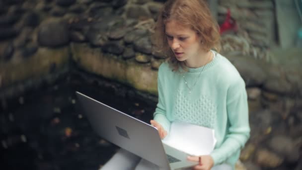 Vrouw met laptop en documenten op de achtergrond van een muur van stonewall — Stockvideo