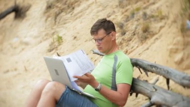 bir telefon bir güneşli gün ve içme şarap cam sahilde denizin kenarında oturan bir çağrı için malzeme çekme iş kağıtları ile bir dizüstü bilgisayarda çalışma meşgul olgun adam