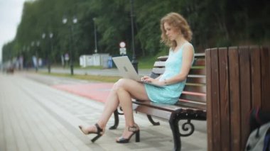 Sahilde bir dizüstü bilgisayar kullanarak bir bankta oturan bir kadın