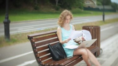 Sahilde bir dizüstü bilgisayar kullanarak bir bankta oturan bir kadın