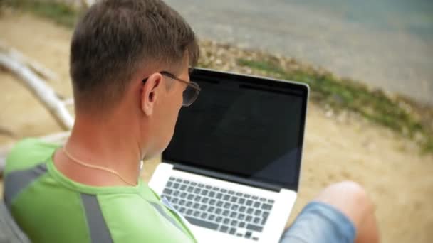 Zajęty dojrzały człowiek działa na komputerze przenośnym z dokumentami firmy zbierając telefon do pracy wywołanie siedzi na plaży nad morzem na słoneczny dzień i picia wina ze szkła — Wideo stockowe