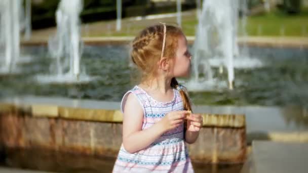 Dziecko, mała dziewczynka jedzenie Ice Cream na ciepłej, upalny letni dzień, dzieci w pobliżu fontanny — Wideo stockowe