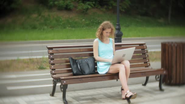 Een vrouw zitten op een bankje op het strand met behulp van een laptop — Stockvideo