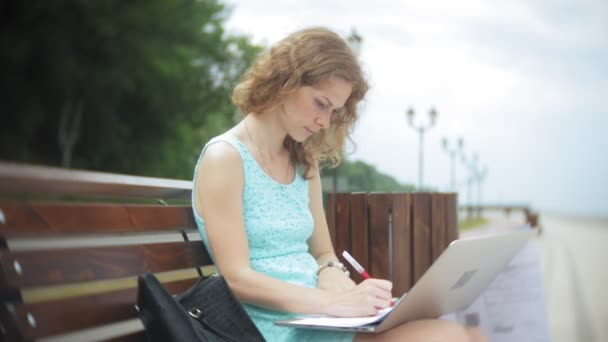 Kobieta siedzi na ławce na plaży przy użyciu laptopa — Wideo stockowe