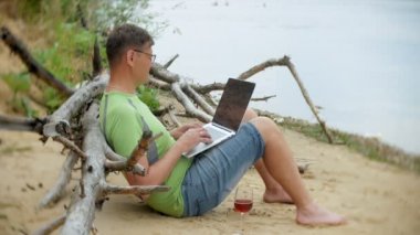 bir telefon bir güneşli gün ve içme şarap cam sahilde denizin kenarında oturan bir çağrı için malzeme çekme iş kağıtları ile bir dizüstü bilgisayarda çalışma meşgul olgun adam