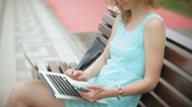 Sahilde bir bankta oturan bir kadın bir dizüstü bilgisayar okuma belgeye sahiptir