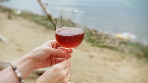 유리에서 와인을 마시는 바다의 모래 해변을 따라 걷는 젊은 아름 다운 여자 — 비디오