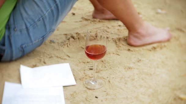 Beschäftigter älterer Mann, der an einem Laptop arbeitet, auf dem Geschäftspapiere liegen und zum Telefon greift, um an einem sonnigen Tag am Strand am Meer zu telefonieren und Wein aus einem Glas zu trinken — Stockvideo