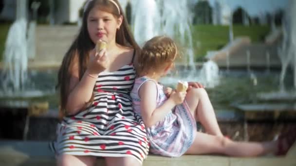 Gyermek, a kis lány eszik fagylaltot egy forró, perzselő nyári nap, a gyermekek közelében a kút — Stock videók