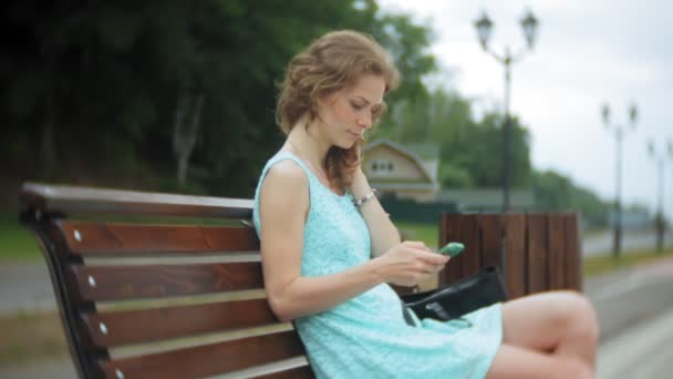 En kvinna sitter på en bänk på stranden med en bärbar dator — Stockvideo