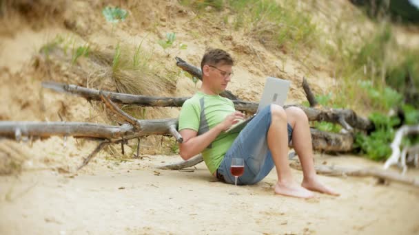 晴れた日のガラスからワインを飲んだり、海のビーチで座って呼び出しを動作するように携帯電話を拾ってビジネス紙でラップトップ コンピューターに取り組んで忙しい中年の男性 — ストック動画