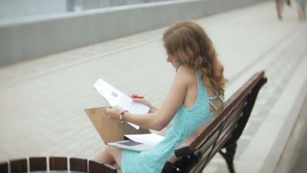 浜辺のベンチに座っている女性が読む文書のノート パソコンを楽しんでいます — ストック動画
