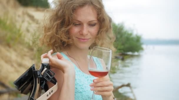 Mooie jongedame wijn drinken uit een glas en wandelen langs het zandstrand van de zee — Stockvideo