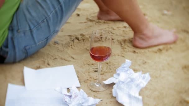 Drukke volwassen man aan het werk op een laptopcomputer met handelspapieren oppakken van een telefoon om te werken een oproep zittend op het strand aan zee op een zonnige dag en drinken wijn uit een glas — Stockvideo