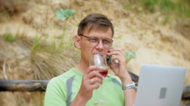 bir telefon bir güneşli gün ve içme şarap cam sahilde denizin kenarında oturan bir çağrı için malzeme çekme iş kağıtları ile bir dizüstü bilgisayarda çalışma meşgul olgun adam