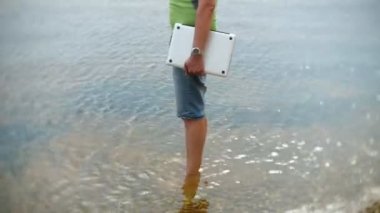 Bir adam sahilde bir dizüstü bilgisayar ile su yaz aylarında duruyor