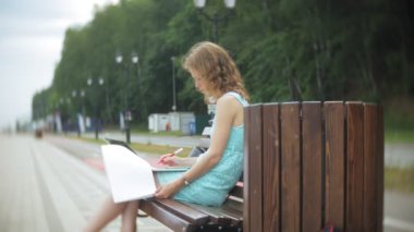 Sahilde bir bankta oturan bir kadın bir dizüstü bilgisayar okuma belgeye sahiptir