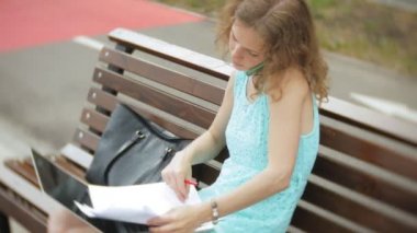 Sahilde bir bankta oturan bir kadın bir dizüstü bilgisayar okuma belgeye sahiptir